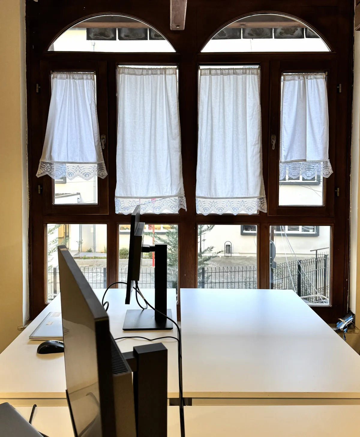 Desks with monitors beside tall arched windows